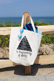 "buyerarchy" tote with a ocean background on a wood fence with sunglasses and a towel. Buyerarchy is a pyramid reading from top down "buy, make, thrift, swap, borrow, use what you have" then underneath the pyramid "the buyerarchy of needs"