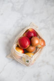 Lifestyle photo of a natural colored mesh produce bag with apples and onions peeking out.